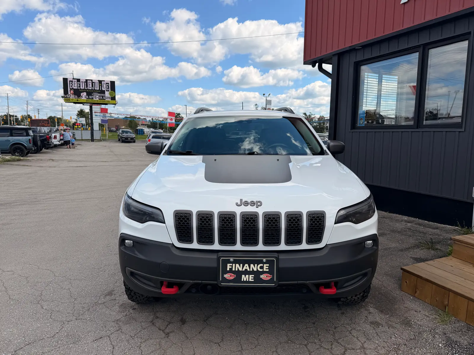 2021 Jeep Cherokee Trailhawk White front exterior view with distinctive seven-slot grille and red tow hooks at dealership lot.