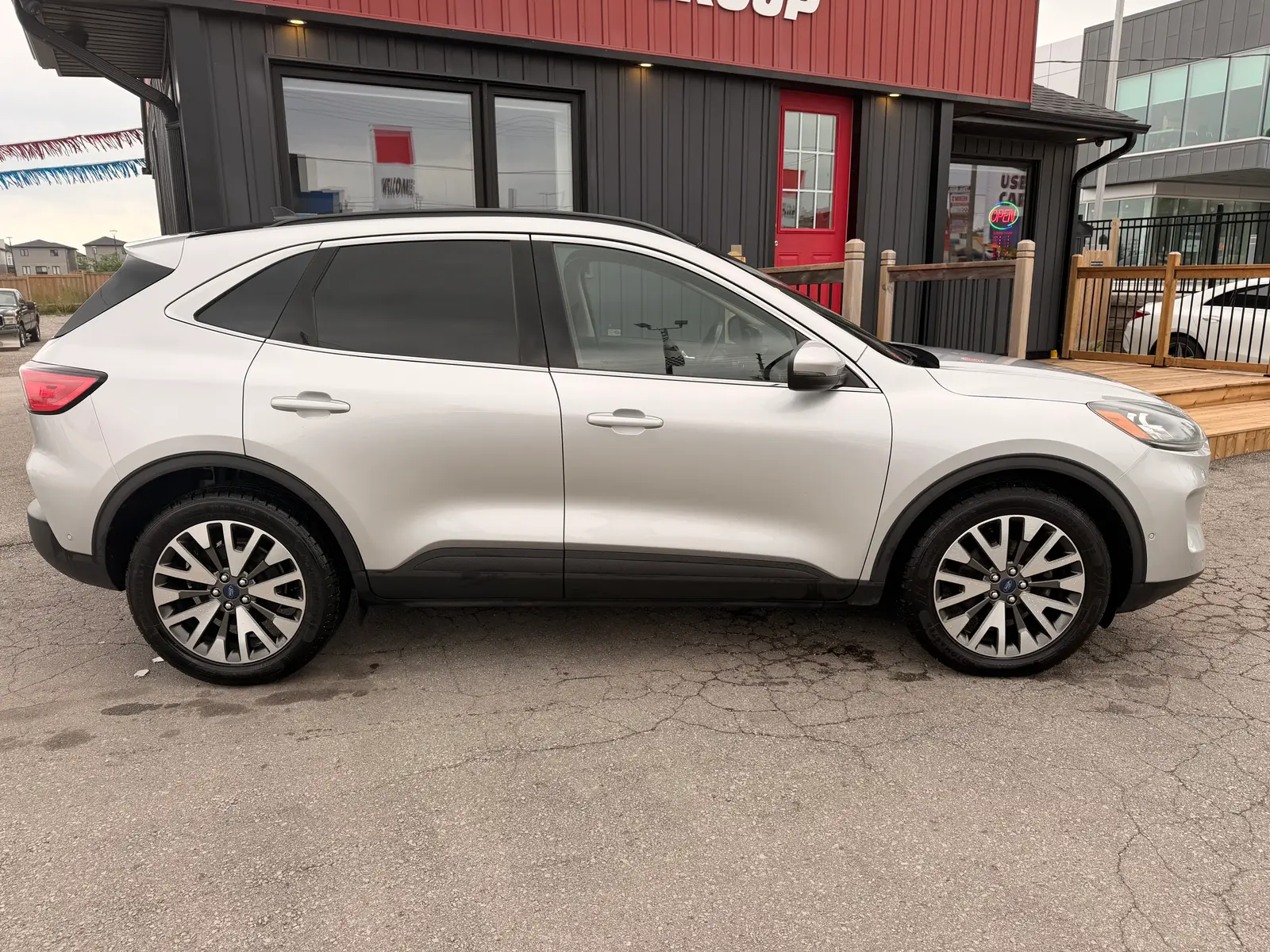 2020 Ford Escape Titanium Silver driver side exterior view with multi-spoke alloy wheels parked at commercial storefront.